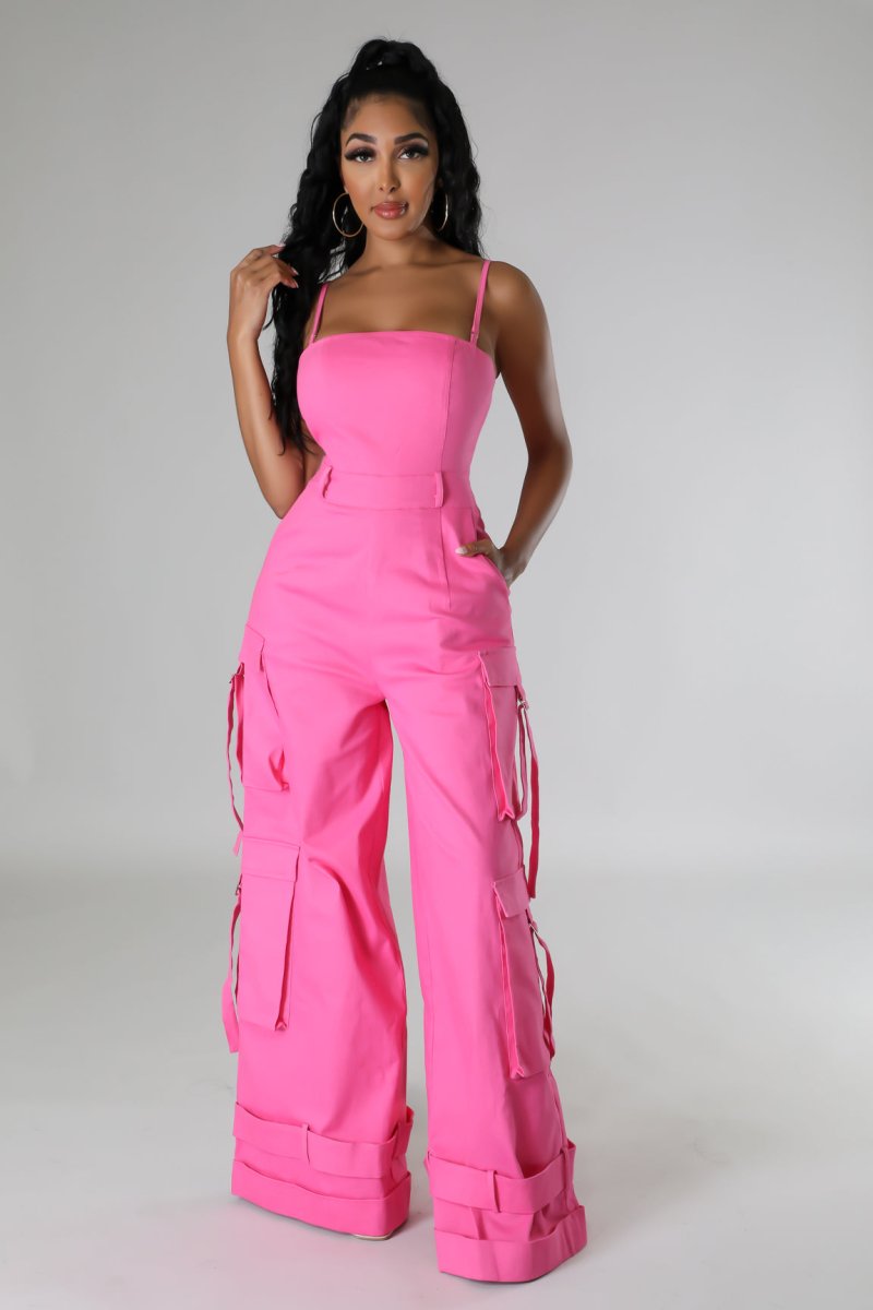 A model wearing a pink non-stretch jumpsuit with spaghetti straps, a square neckline, pockets, and wide-leg design.