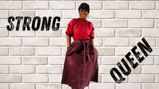 Woman in red top and patterned skirt standing against a brick wall with 'STRONG QUEEN' text.