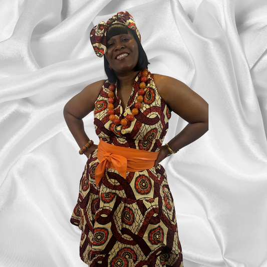 A woman standing in front of a white silky background, wearing an African print dress with a smile on her face.